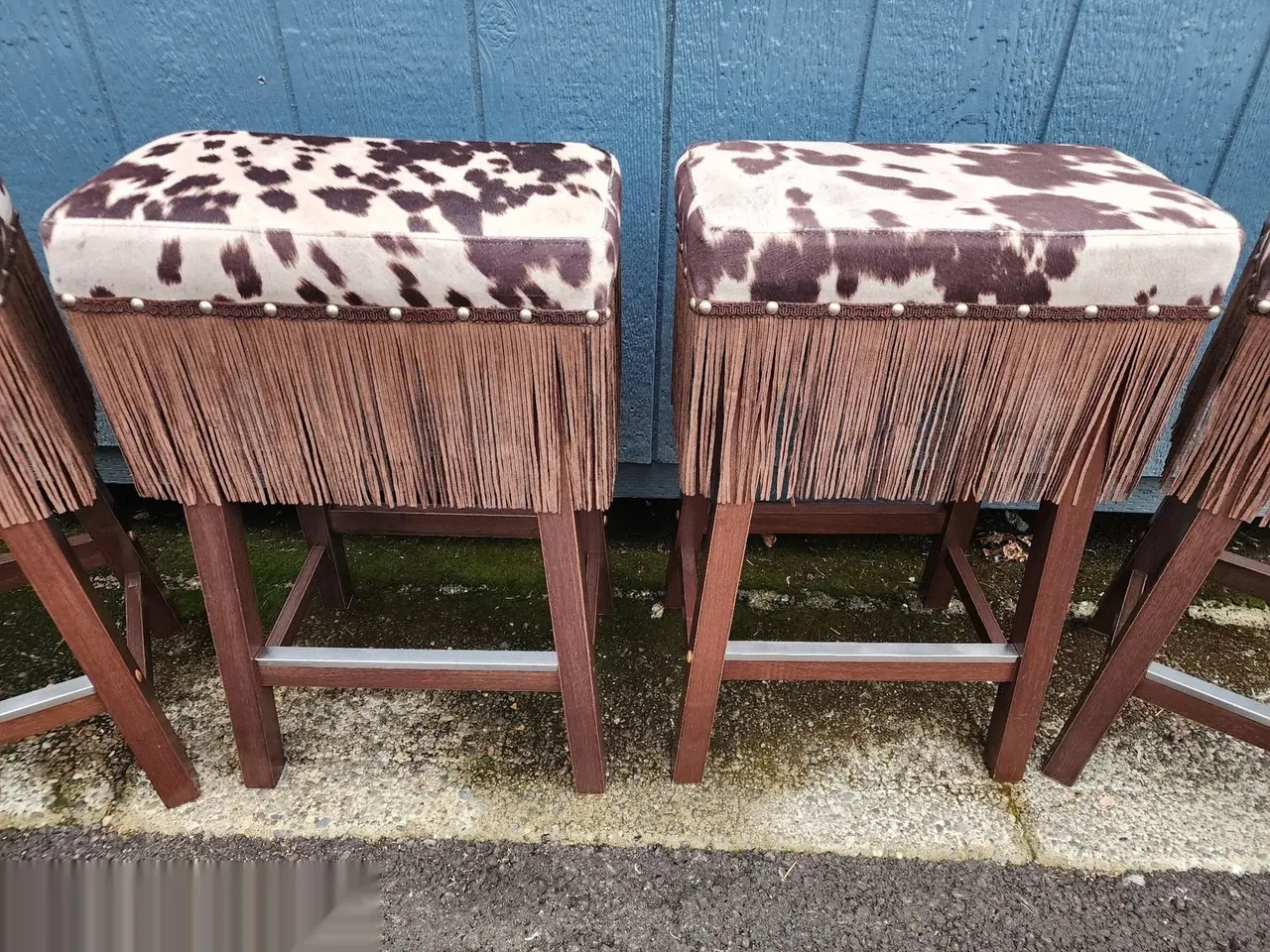 Pair of ottomans reupholstered in cowhide-print fabric with fringe trim.