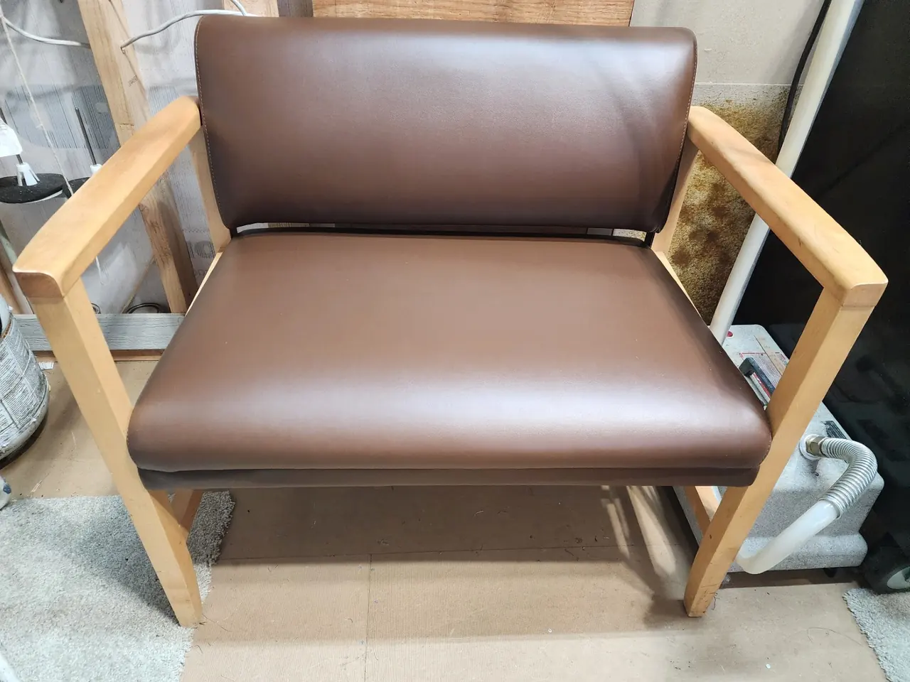 Close view of a commercial waiting room bench reupholstered in brown vinyl with a wood frame.