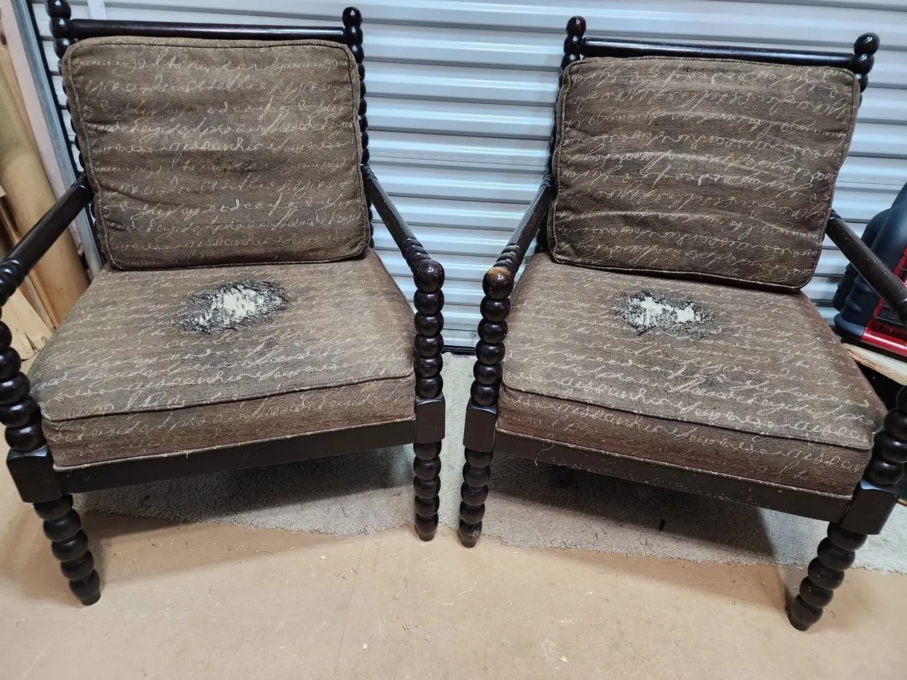 Pair of spool-leg accent chairs in worn script-print fabric before restoration.
