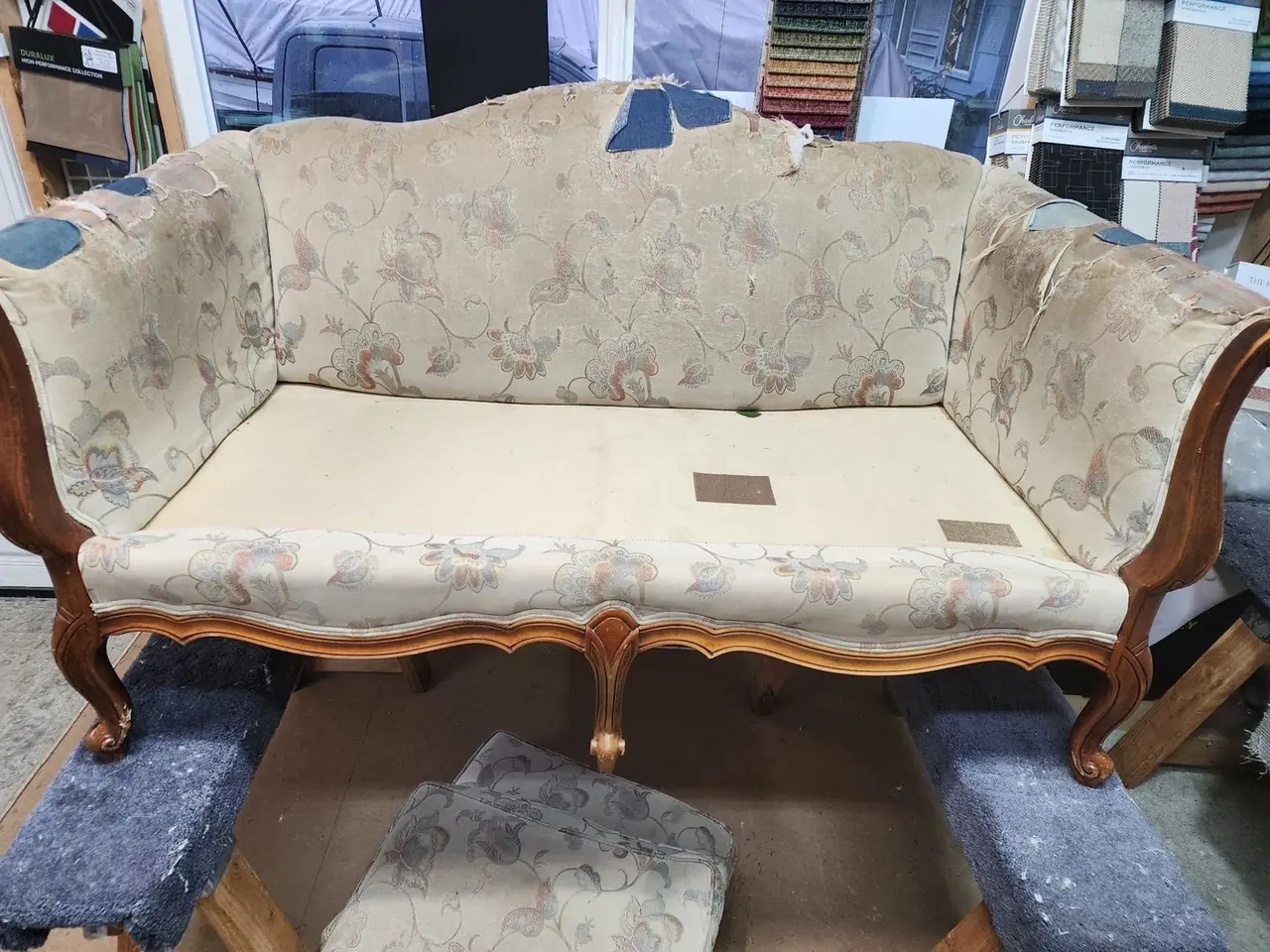 Antique loveseat in worn cream floral fabric before restoration.
