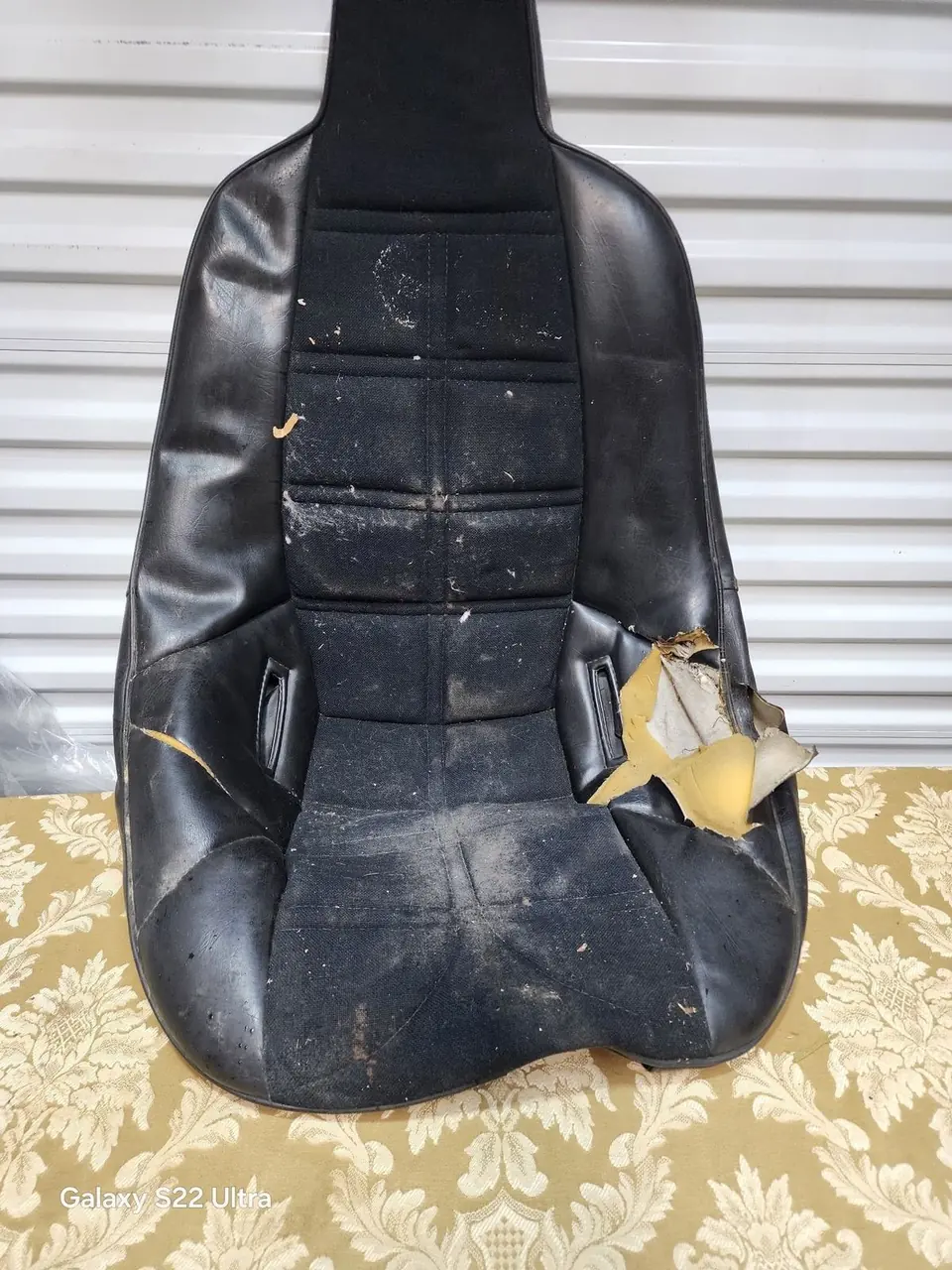 Worn and torn black vinyl bucket seat before restoration, foam exposed.