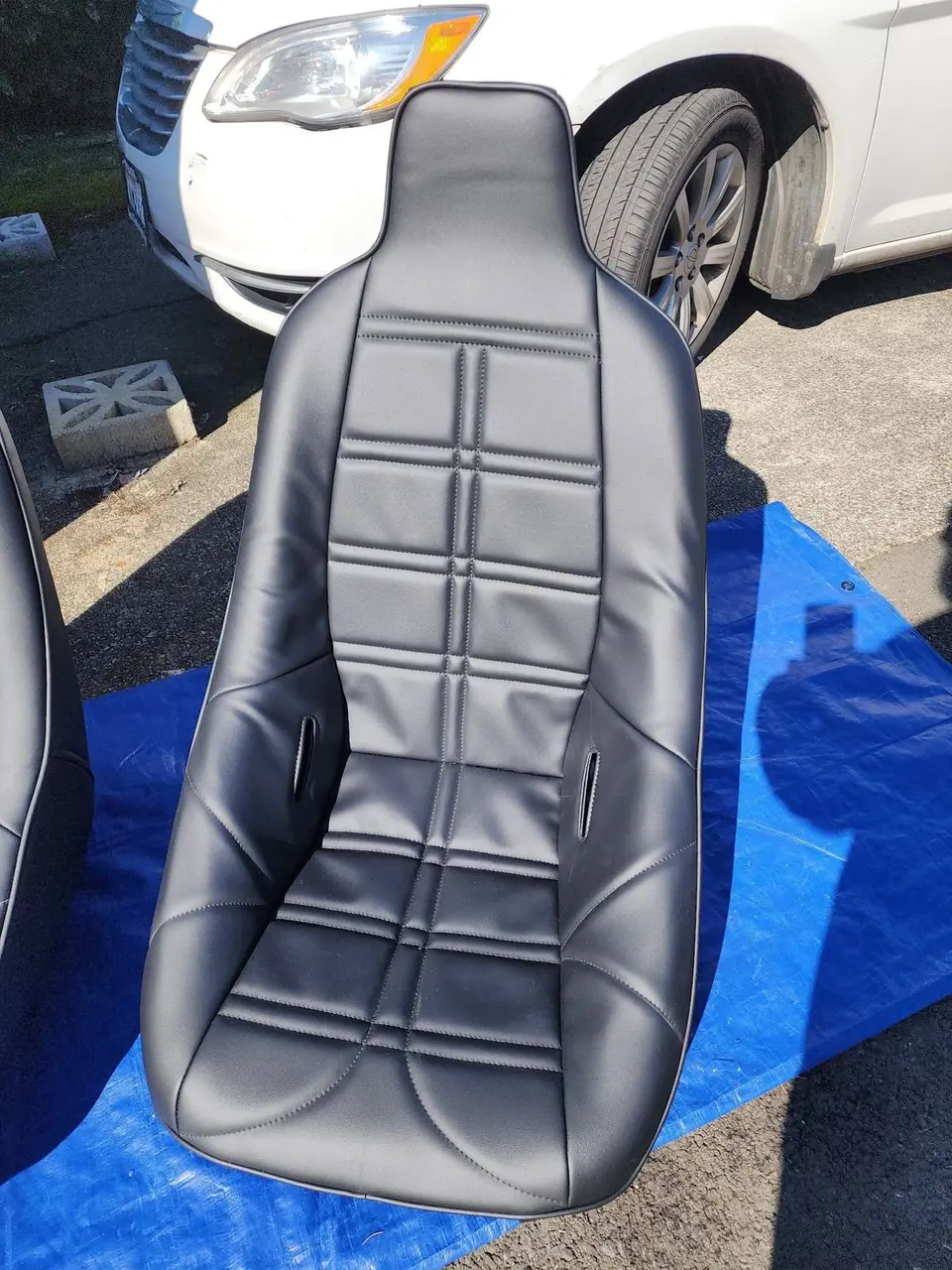 Black quilted automotive racing seat, freshly upholstered, parked next to a car.