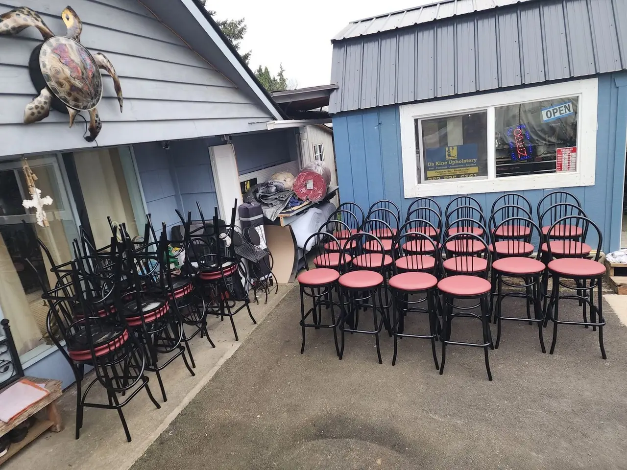 Batch of restaurant bar stools and chairs, worn maroon seats stacked next to freshly reupholstered coral seats.