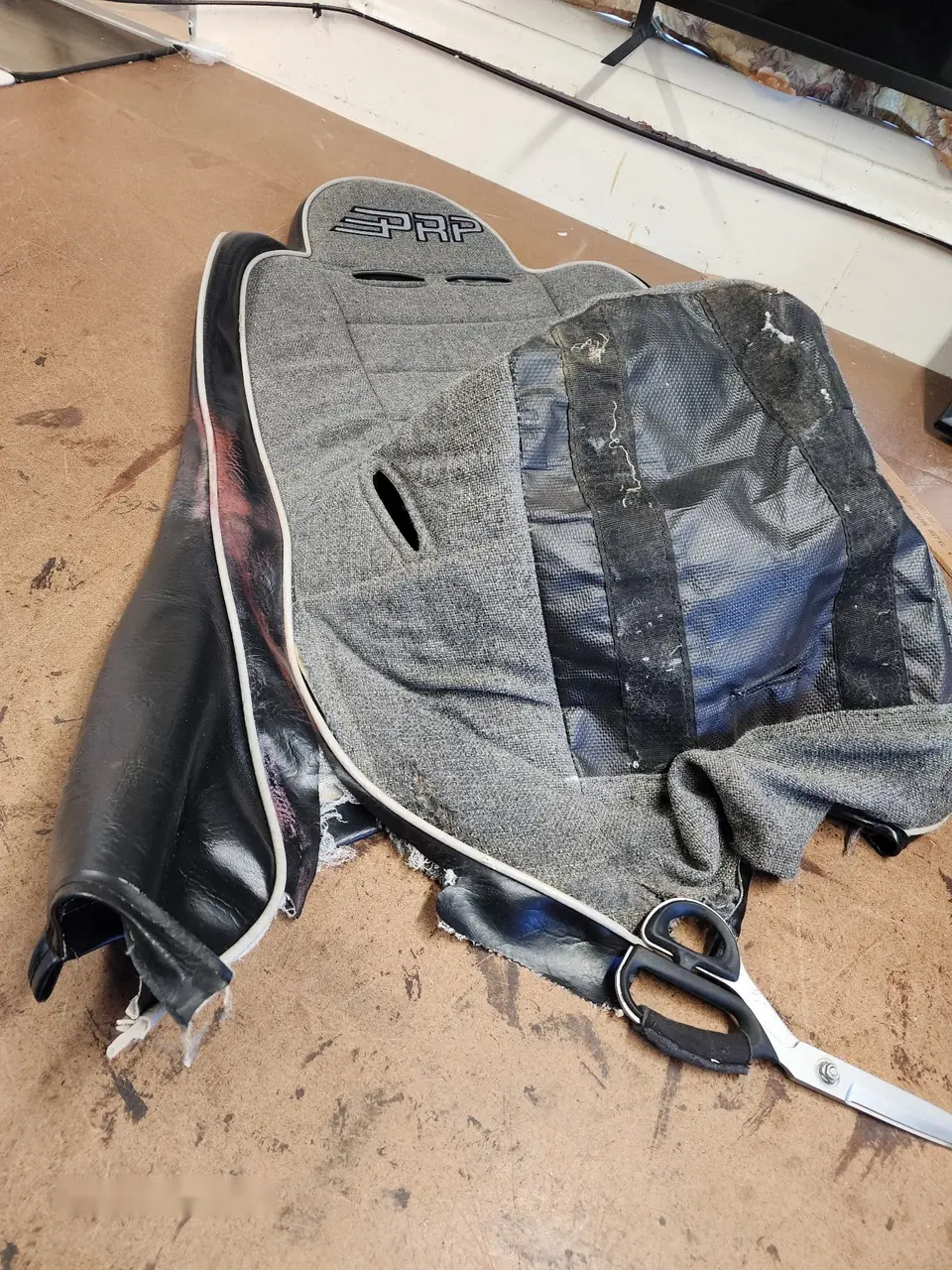 Torn PRP gray fabric and black vinyl bucket seat cover removed for restoration.