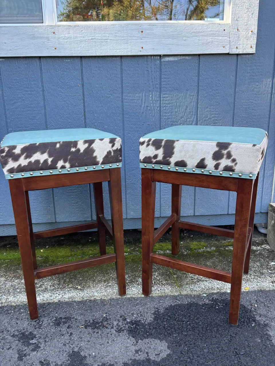 Pair of wood barstools reupholstered in cowhide print with turquoise leather trim and nailhead detailing.